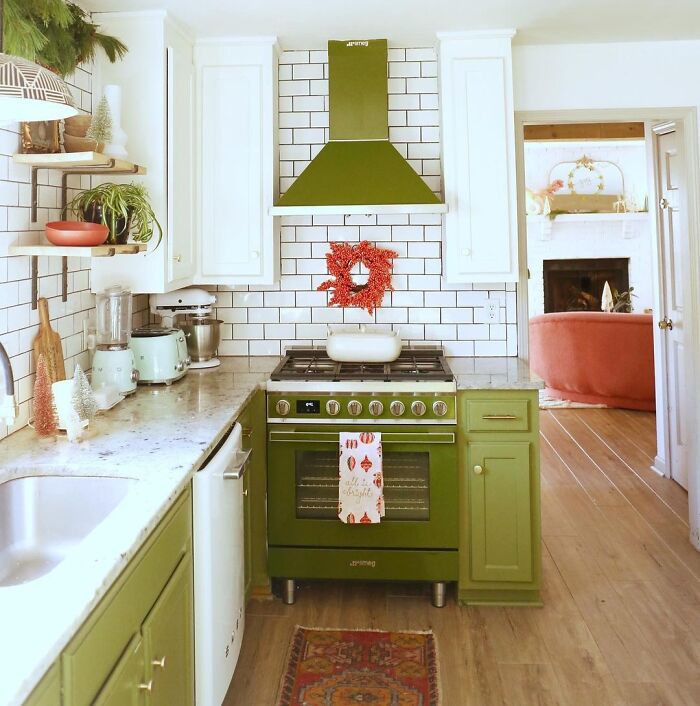 Green kitchen cabinets with marble countertops and matching green range hood in a bright natural light kitchen.
