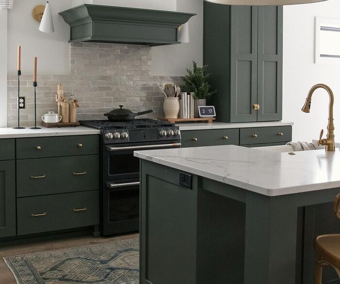 Dark green kitchen cabinets with white marble countertops and brass fixtures in a modern home kitchen design.