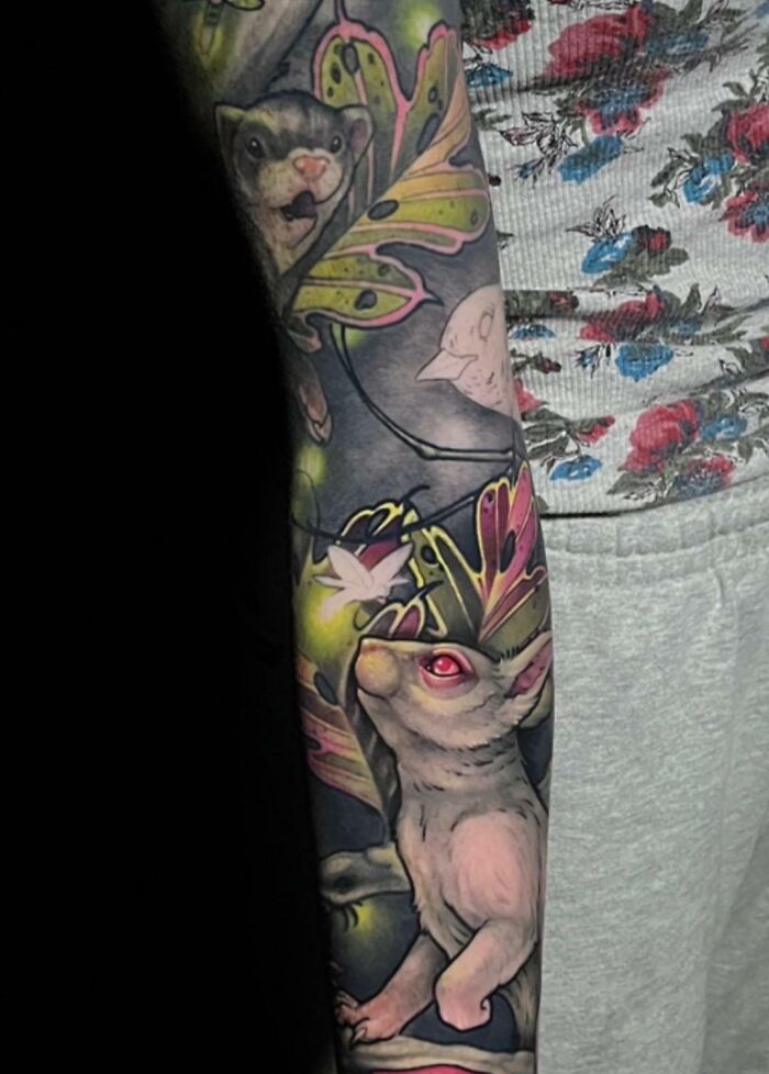 Colorful animal tattoo featuring a rabbit with red eyes and foliage details on an arm.