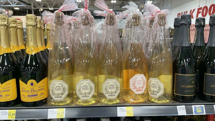 Bottles of champagne wrapped in loose plastic bags on a store shelf illustrating packaging fails.
