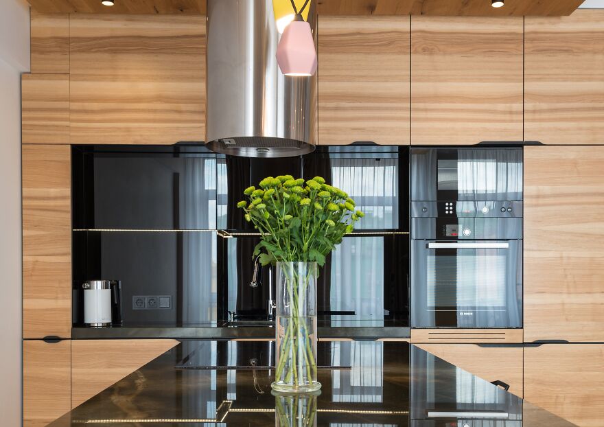 Wooden modern kitchen cabinets with built-in appliances and a stainless steel range hood in a stylish kitchen design.