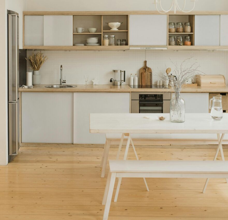 Dining table with a vase in front of modern and stylish kitchen cabinets in wooden and white colors.