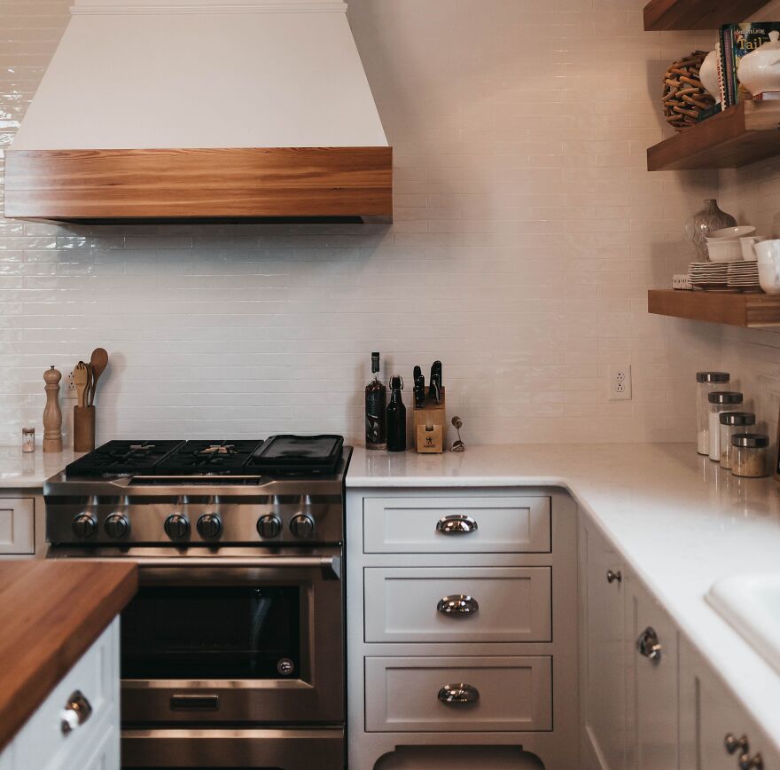 White and wooden kitchen cabinets with stainless steel stove and white tiled backsplash in a modern kitchen design