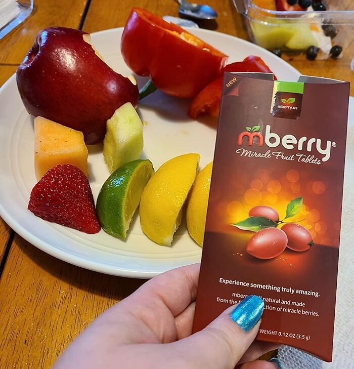 mberry Miracle Fruit Tablets on table with assorted fruits, including red apple, lemon, lime, strawberry, and bell pepper.