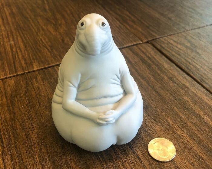 Unique gift for weirdo friends: quirky blob figure next to a coin for scale on a wooden table.