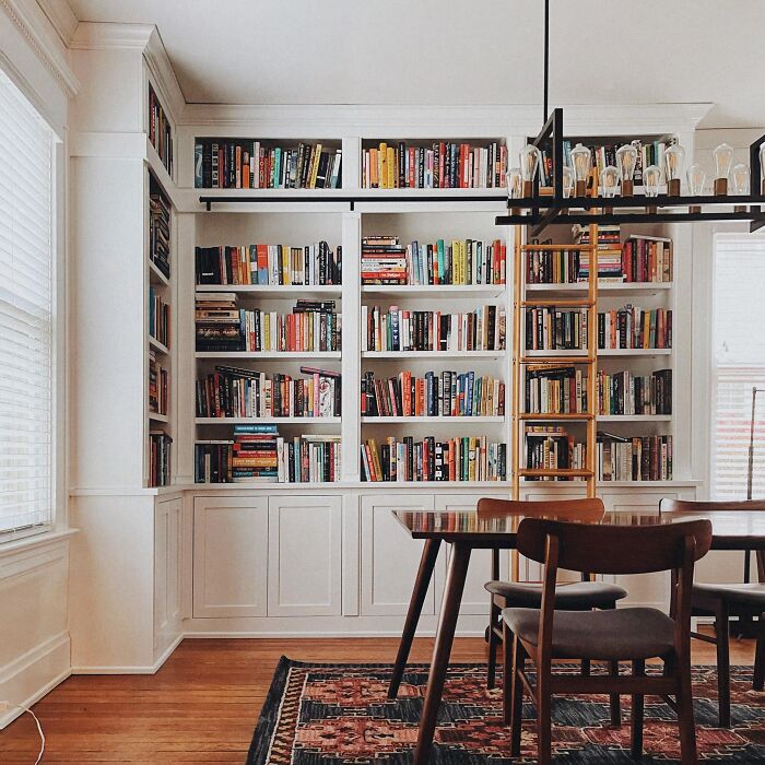 Dining room with white bookshelves, wooden table and chairs, and a patterned rug for family gatherings and parties.