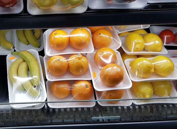 Packaged bananas, oranges, and lemons in plastic wrap and foam trays showcasing facepalm-worthy packaging fails.