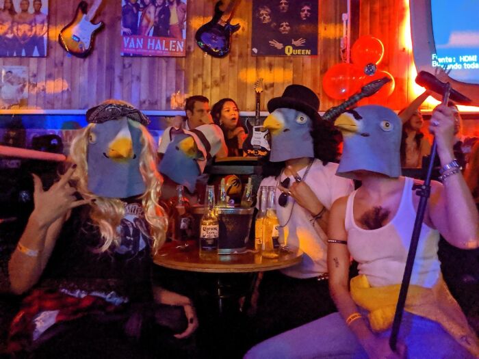 People wearing bird masks in a quirky bar setting, showcasing unconventional gifts for weirdo friends.