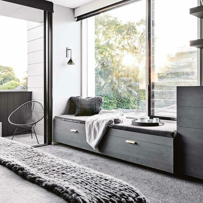 Grey and simple window seat nook with cushions and soft throw, creating a cozy and inviting space by the large glass window.