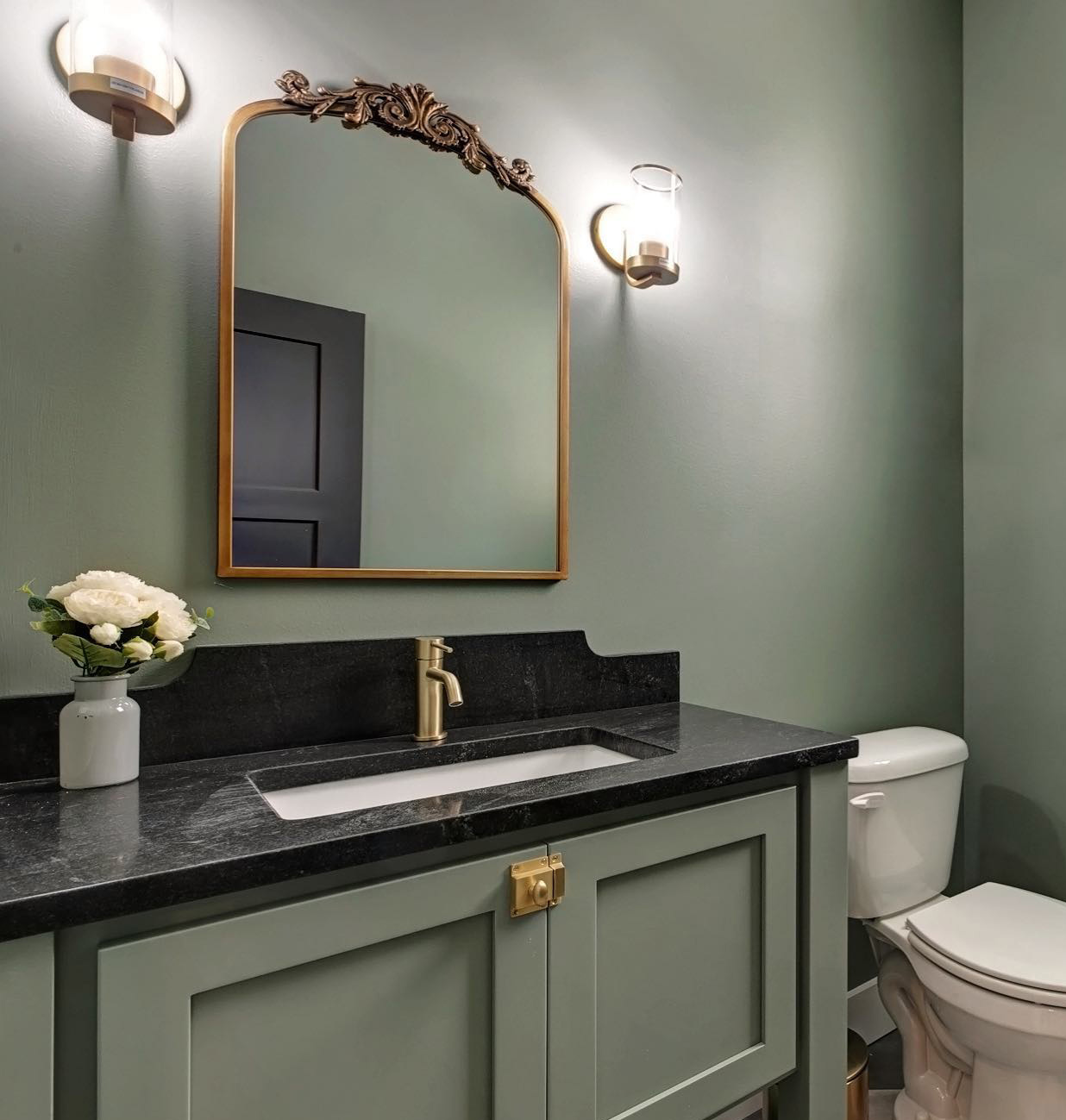 Grayish green bathroom with same color cabinets, mirror and flower decor