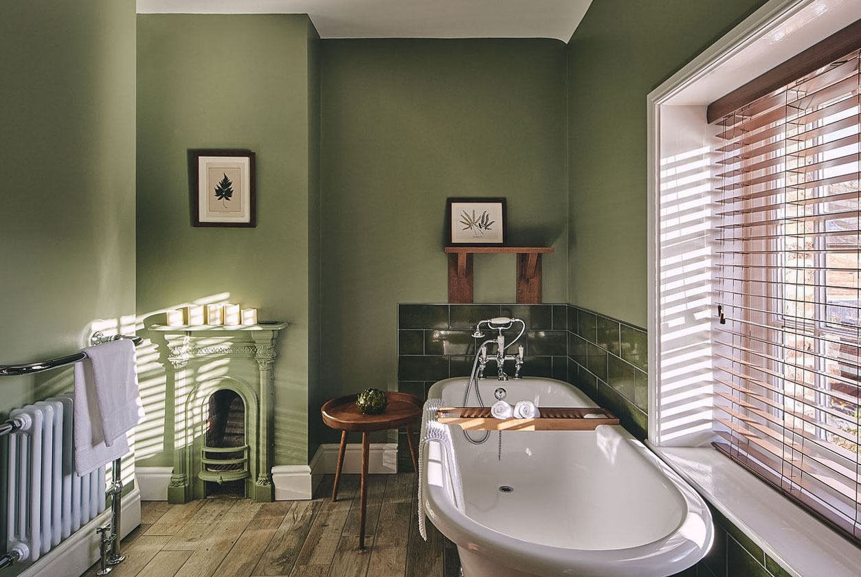 Green bathroom with wooden floor, tiles, wall art, and bathtub