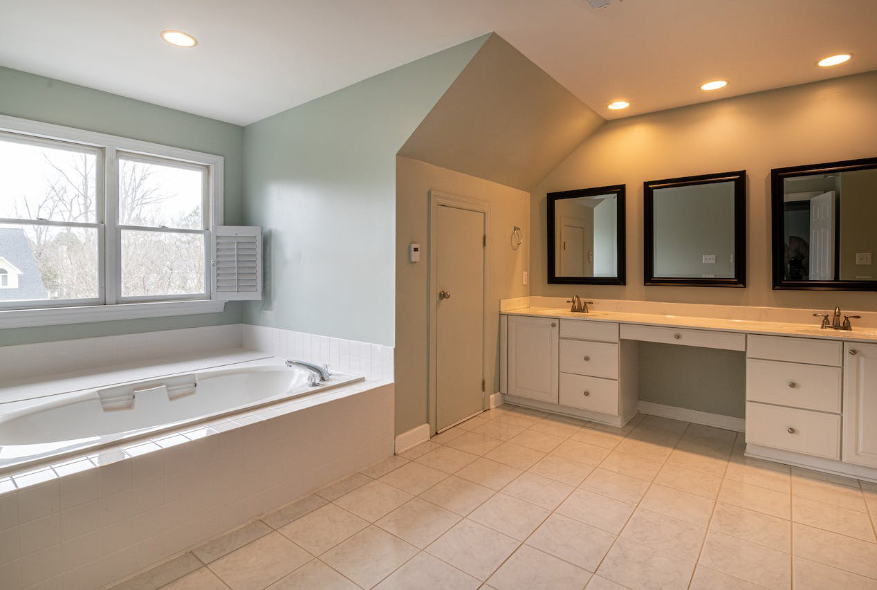 Light green bathroom with window, tiled floor, and three mirrors