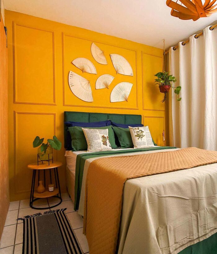 Bedroom featuring yellow wainscoting panels with white folding fans wall art and green and mustard bedding accents.
