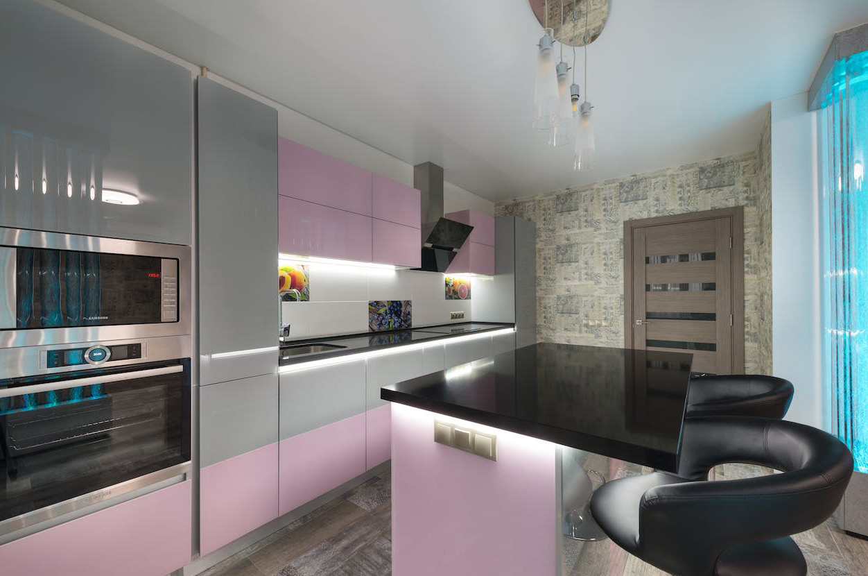Modern kitchen featuring black polished concrete countertops with light pink and gray cabinets and seating area