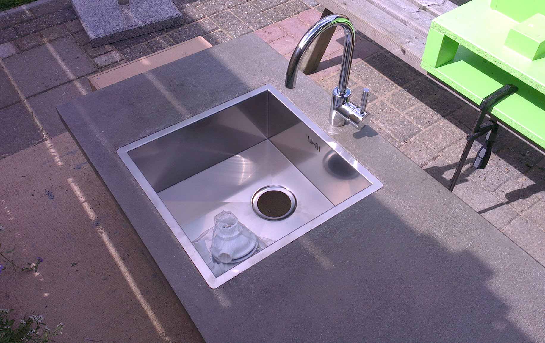 DIY concrete countertops with a built-in stainless steel sink and faucet outdoors on a paved surface.