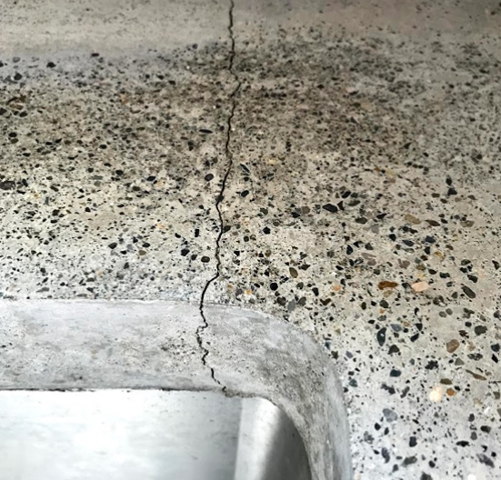 Close-up of a DIY concrete countertop with a visible crack near the kitchen sink edge, highlighting durability issues.