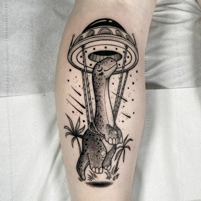 Dinosaur tattoo depicting a UFO abducting a Brachiosaurus, featuring detailed black ink design with palm trees.