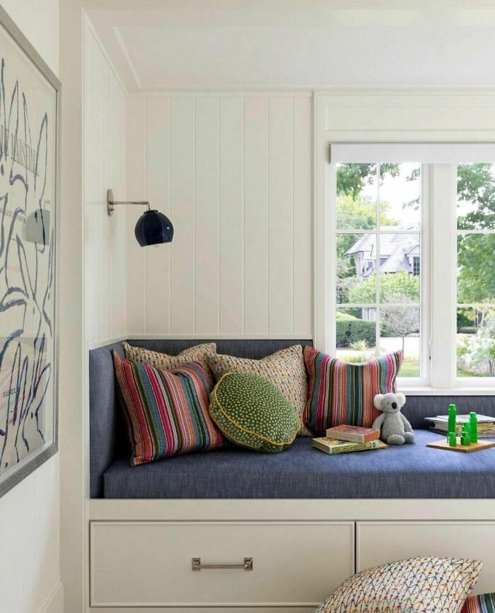 Colorful and bright window seat nook with patterned cushions, a teddy bear, and natural light for a cozy home space.