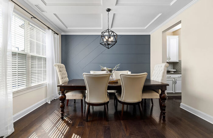 Dining room with white wainscoting panels on the ceiling and a gray accent wall, featuring classic furniture and natural light.