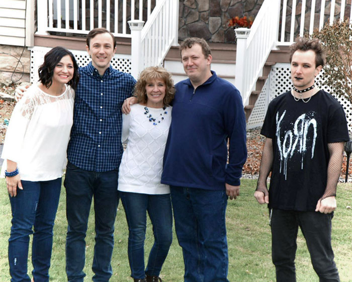 Family posing for a photo outside a house, one person wearing a contrasting Korn band T-shirt.