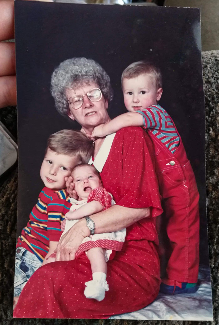Elderly woman in glasses holding three children, capturing a funny yet awkward family photo moment.