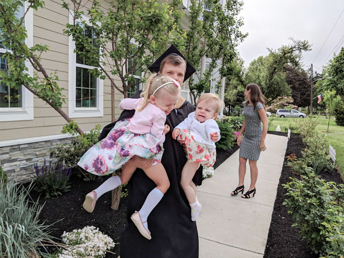 Graduate holding crying toddlers, creating an embarrassing yet hilarious family photo.