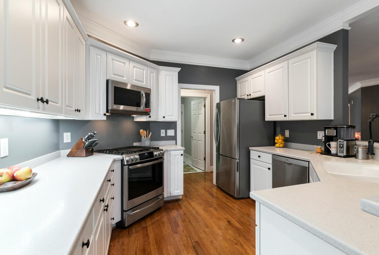 White kitchen featuring honed concrete countertops with gray walls and stainless steel appliances in a modern style.