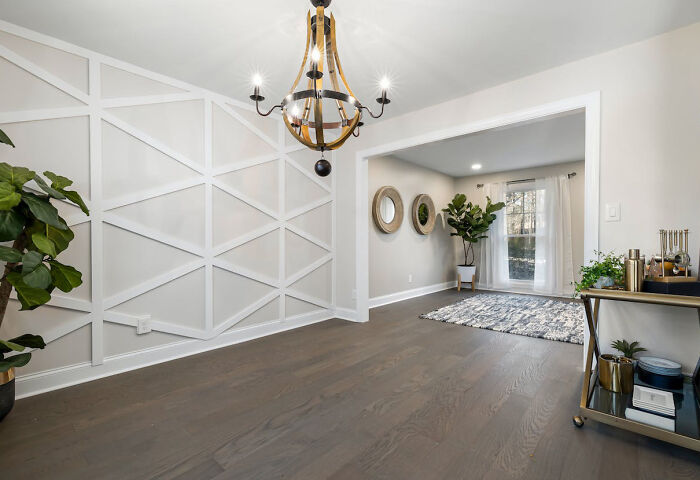 Interior featuring light geometric wainscoting panels, hardwood floors, modern chandelier, and stylish decor elements.