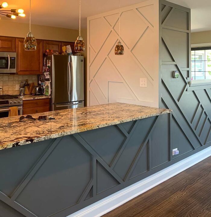 Kitchen with geometric abstract wainscoting panels in dark and light colors beside granite countertop and wood flooring
