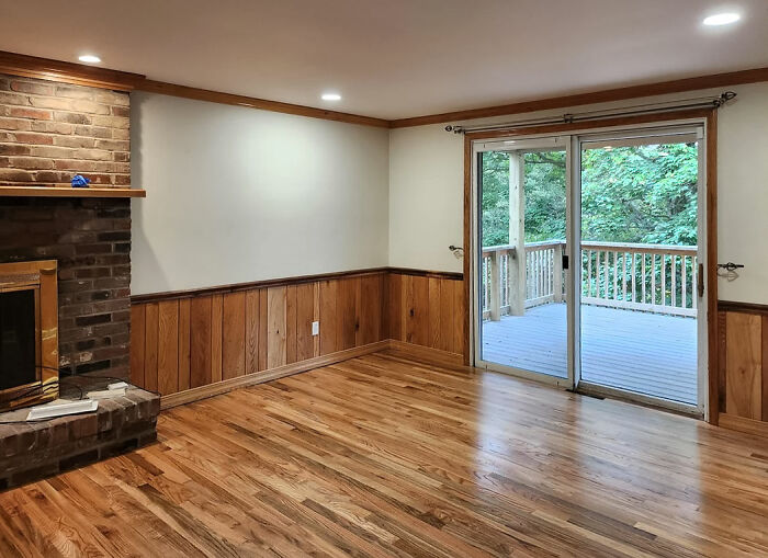 Living room with wood flooring, brick fireplace, and natural wood wainscoting panels along the walls near sliding glass doors.