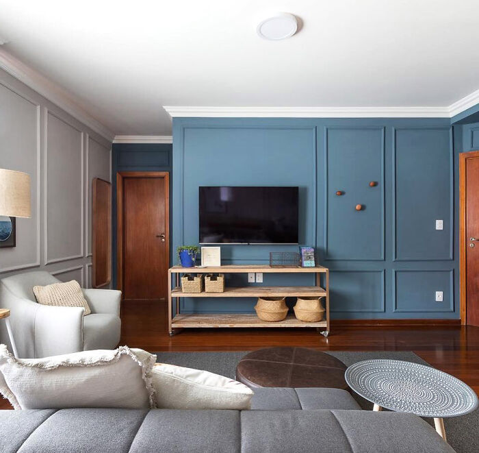 Living room with picture frame wainscoting panels, gray sofa, TV on blue accent wall, and wooden furniture.