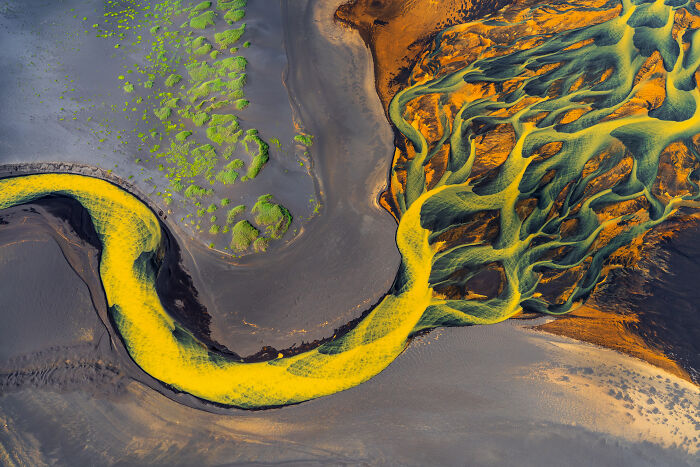 Aerial view of a colorful nature scene showing vibrant yellow and green river patterns in the 2023 winning nature images.