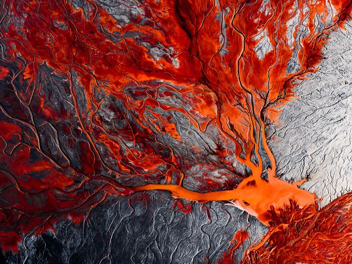 Abstract aerial shot of vibrant red-orange lava flow patterns in winning nature images from 2023 International Photography Awards.