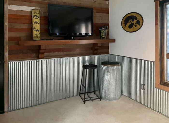 Room interior featuring metal wainscoting panels, reclaimed wood flooring on walls, and a mounted flat-screen TV.