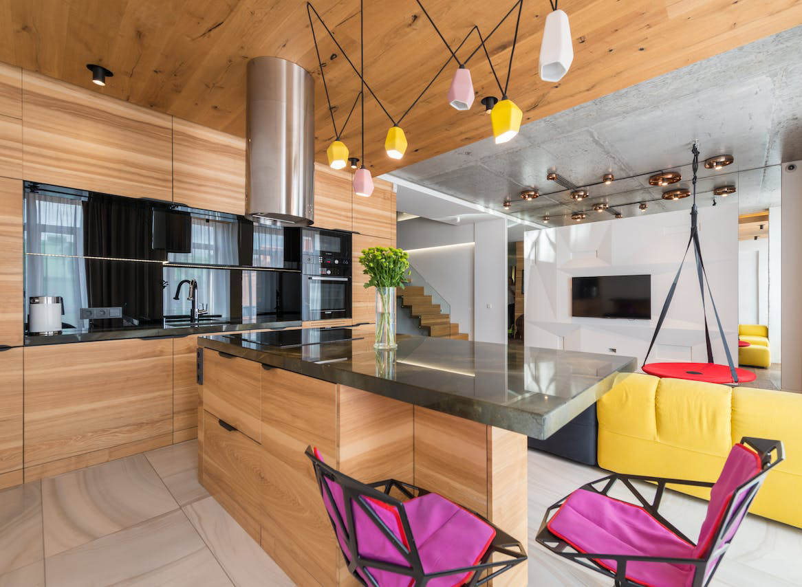 Modern kitchen featuring wooden cabinets and a polished concrete countertop with colorful seating and lighting.