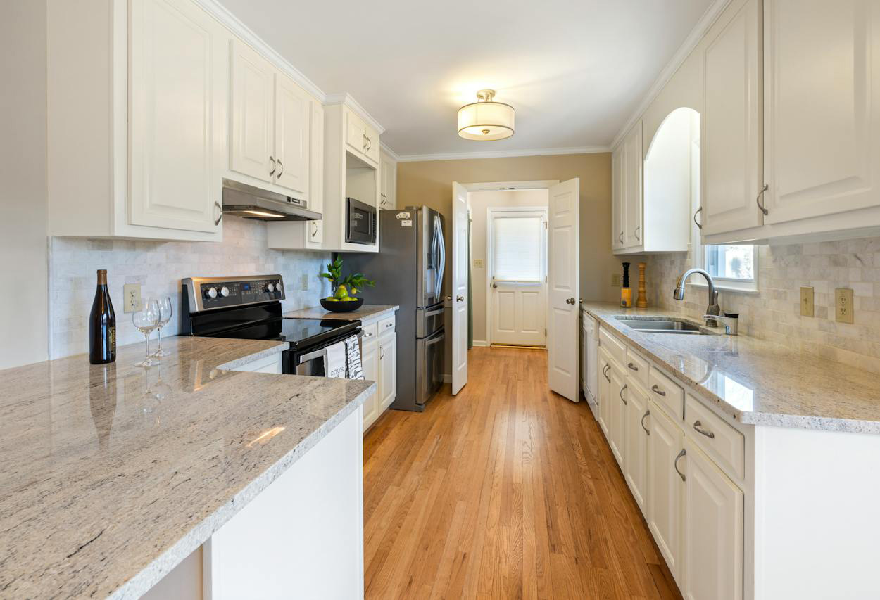 White kitchen featuring recycled concrete countertops with modern appliances and natural hardwood flooring in a bright space