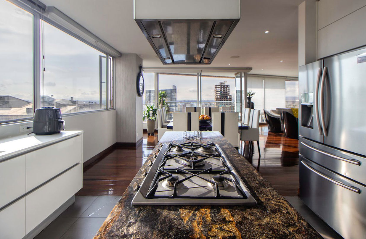 Modern kitchen with large windows, silver fridge, and stamped concrete countertop featuring built-in gas stove burners