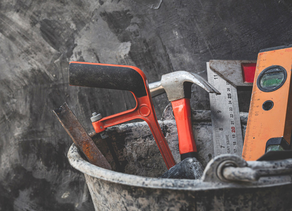 Various tools with orange handles in a bucket, used for working with concrete countertops during kitchen projects.