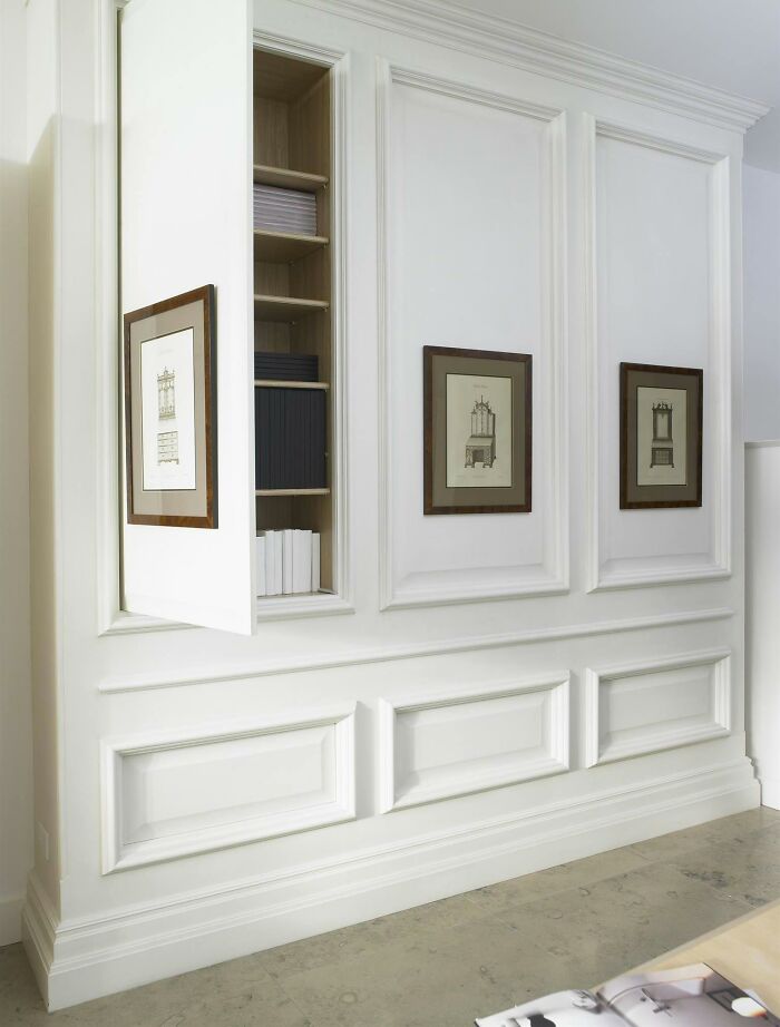 White wainscoting panels with built-in hidden storage and framed wall art in a modern home interior.