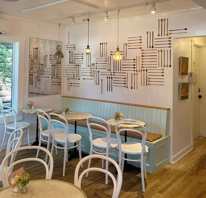Spoon wall art arranged in a geometric pattern on a white wall above a stylish café seating area in a cozy space.