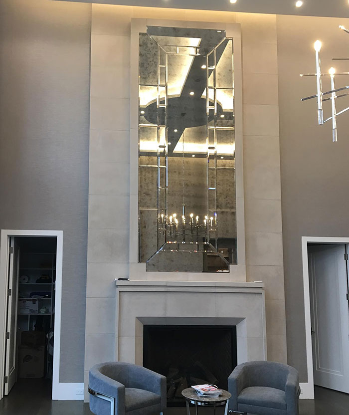 Massive antique mirror above fireplace mantel reflecting chandelier in a stylish space with creative wall art ideas.