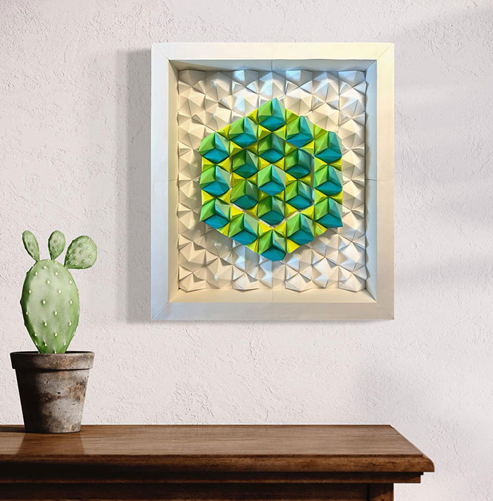 Colorful framed paper wall art decor with geometric design displayed above wooden table and potted cactus plant.