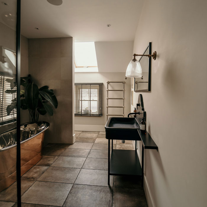 Light beige bathroom with tiled floor, black sink, metal tub and a plant