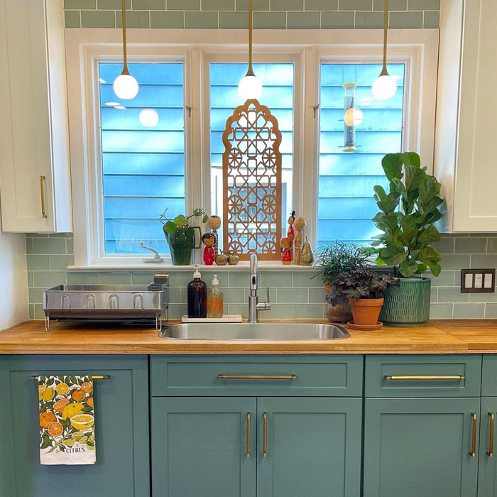 Green kitchen cabinets with butcher block countertop, stainless steel sink, and decorative plants by a window. Green kitchen cabinets with butcher block countertop, stainless steel sink, and decorative plants by a window.