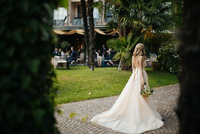 Bride in a wedding dress holding bouquet, walking alone on garden path, hinting at potential divorce signs at weddings.