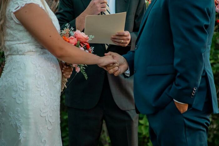 Couple holding hands during wedding ceremony with officiant reading vows, hinting at potential divorce signs.