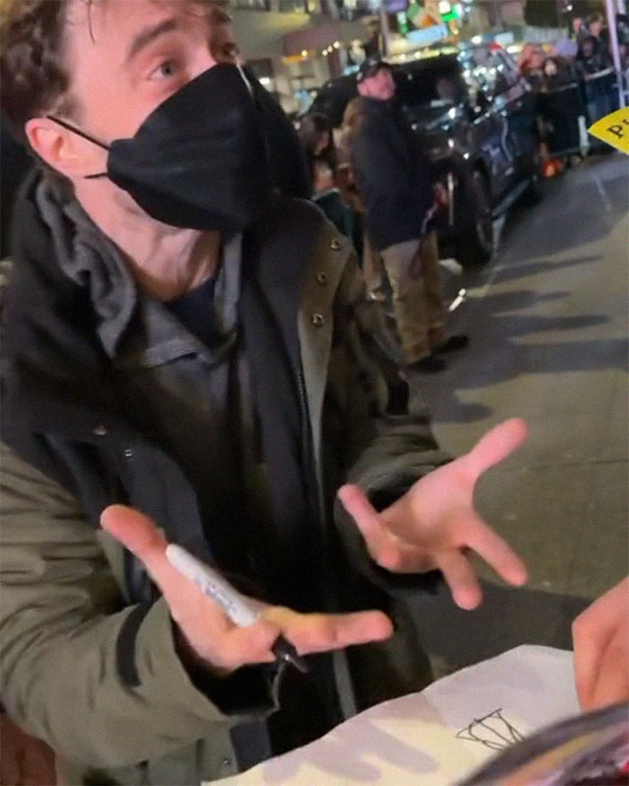 Daniel Radcliffe in a mask gestures with a pen, possibly discussing a Deathly Hallows drawing outside. Daniel Radcliffe in a mask gestures with a pen, possibly discussing a Deathly Hallows drawing outside.