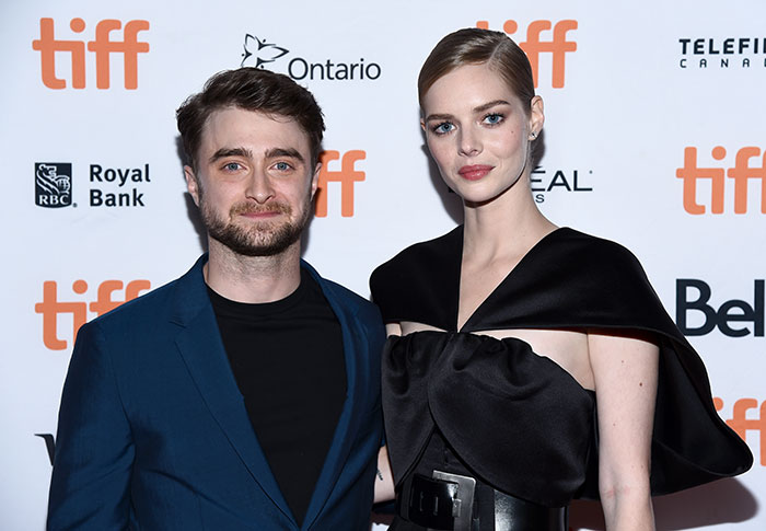 Daniel Radcliffe at TIFF event, posing with a co-star, discussing his Deathly Hallows drawing and fan tattoos. Daniel Radcliffe at TIFF event, posing with a co-star, discussing his Deathly Hallows drawing and fan tattoos.