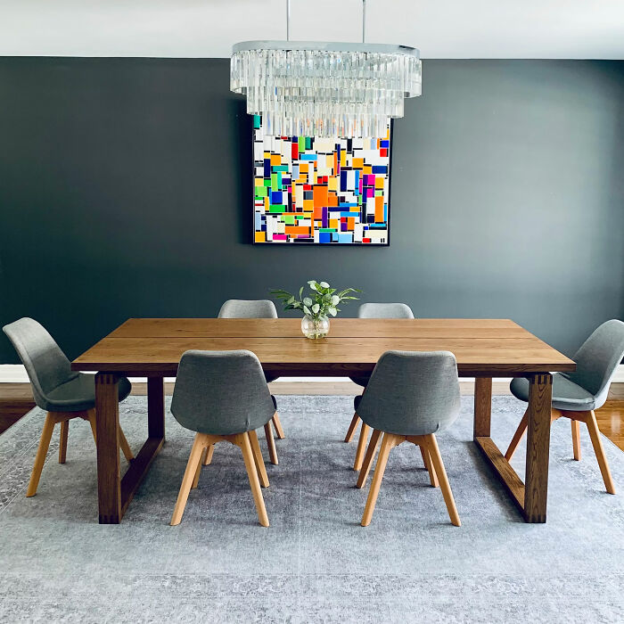 Gray dining room with wooden table, gray chairs, colorful wall art, and modern chandelier showcasing dining room ideas.