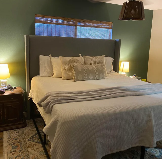 Big bed with light linens near a green wall